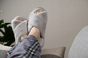 Stylish modern grey house slippers on women's feet lying on sofa