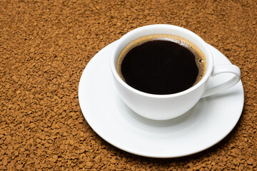 A cup of hot instant coffee on a background of freeze-dried granules