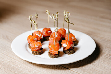 Smoked Salmon Appetizers on Dark Rye Bread. Elegant smoked salmon rolls with cream cheese on dark rye bread, garnished with herbs, served on a white plate.