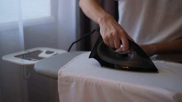 a man ironing a white shirt with an iron close-up of his hands