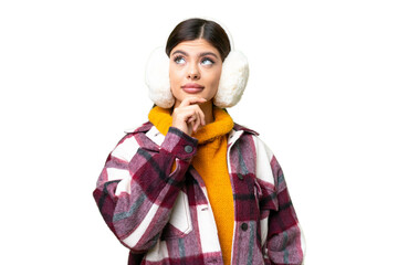 Young Russian woman wearing winter muffs over isolated chroma key background having doubts and with...