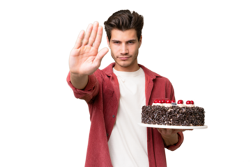 Young caucasian man holding birthday cake over isolated background making stop gesture