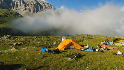 A campsite for overnight camping in the mountains. Orange tent, rucksacks and sleeping bags lying...