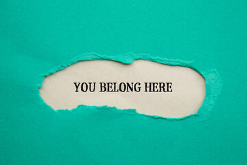 You belong here lettering on ripped blue paper with gray background. Conceptual business photo. Top...