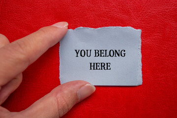 You belong here lettering on ripped paper piece with red background. Conceptual business photo. Top...
