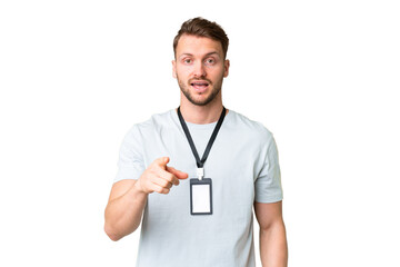 Young caucasian man with ID card over isolated chroma key background surprised and pointing front