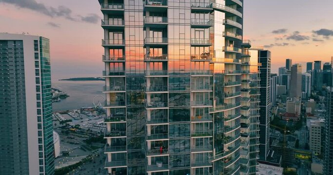 Glass skyscraper in center Miami at sunset against background of Atlantic ocean and promenade with ferris wheel. Reflections in windows of sky. Aerial view of evening city with houses.