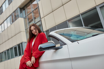 Stylish young woman in red pantsuit leaning against white convertible
