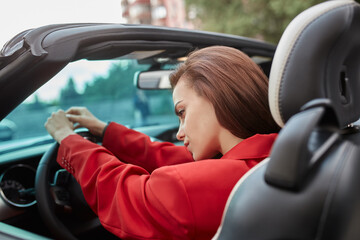 Thoughtful young brunette in red jacket sitting in convertible car