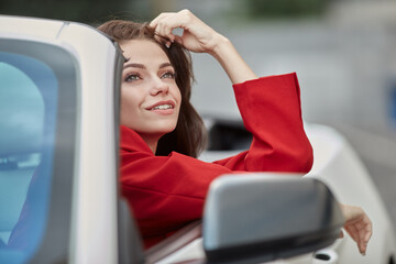 Happy dreamy young brunette looking up to sky in drivers seat of convertible