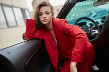 Dreamy young brunette in red blazer sitting in white convertible car