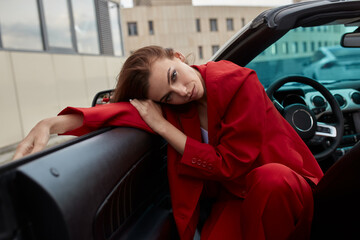 Young brunette in red suit sitting in drivers seat in convertible