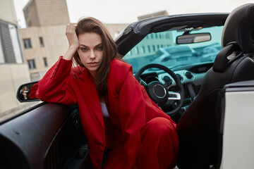 Young woman in red pantsuit sitting in drivers seat of white convertible