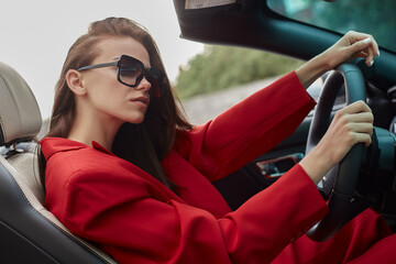 Relaxed young woman in red sitting at wheel in convertible car