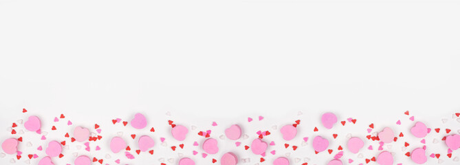Valentines Day bottom border of candy hearts and sprinkles. Top down view on a white banner...