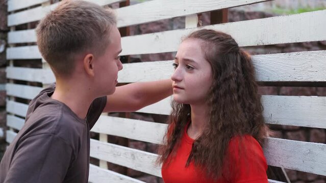 First love, teenage boy pesters girl. Girl is shy and smiles looking at boy.
