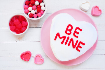 Fun Valentines Day BE MINE heart shaped cake with white icing. Above view over a white wood...
