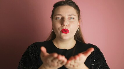 Beautiful woman with makeup and black dress blows kiss, in good mood isolated over pink background. Face, lipstick kiss and beauty woman or makeup model in studio for cosmetics, love and happiness. 