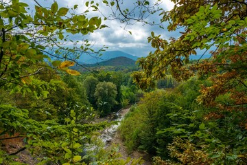 Western Caucasus (South Russia) mountain landscape with a fast river surrounded by green deciduous forest and cumulus clouds on a stormy sky on a summer day