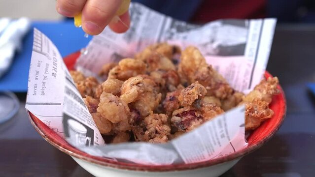 Man squeezing lemon over  Chipirones fritos (Fried baby squid)