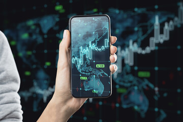 Close up of female hand holding smartphone with growing forex chart arrow and icon on blurry dark background. Financial growth, money and success concept.