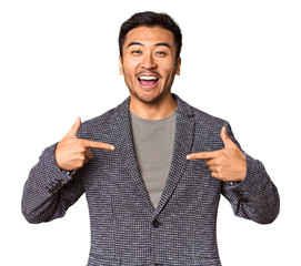 Young Chinese man in studio background surprised pointing with finger, smiling broadly.