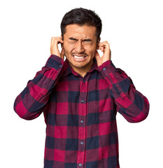 Young Chinese man in studio background covering ears with hands.