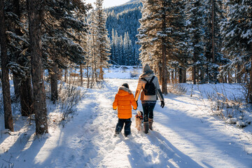 Mother and son walking their dog in a snowy forest on a wintry morning in Alberta, Canada