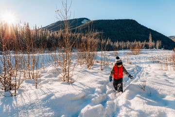 Young boy walking in a snowy landscape on a clear winter morning in Alberta, Canada