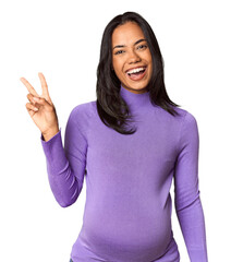 Young Filipina woman expecting a baby in studio joyful and carefree showing a peace symbol with fingers.