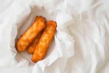 tasty and crunchy fried fish fingers on a white paper, top view