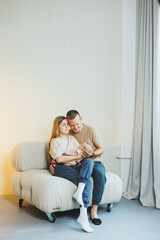 Young happy parents with a newborn baby in their arms at home on the couch. Mom and dad with a newborn baby on a white background