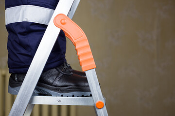 Renovation concept using a metal folding ladder. Worker in uniform on a stepladder makes repairs to the ceiling © malazoniia