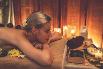 Hot stone massage at spa salon in luxury resort with warm candle light, blissful woman customer...