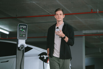 Young man travel with EV electric car to shopping center parking lot charging in downtown city...