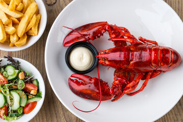 Close up of cooked lobster with fries and side salad in a white bowl on a wooden table in restaurant
