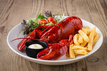 Cooked lobster with fries and side salad in a white bowl on a wooden table in restaurant