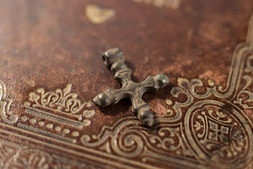 Old cross with patina on antique bible. Christian symbol on the leather cover of the bible.