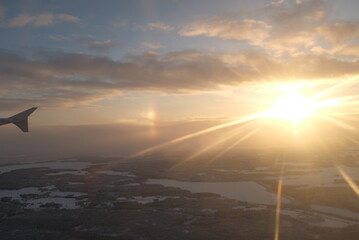 Sun flare shining on a window airplane wing over a winter white landscape over Helsinki, Finland in a winter sunset landscape