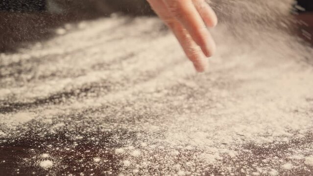 Baker kneading floured dough at bakery. Man sprinkles flour on table. Making bread, bread production. Homemade bakery concept. Close-up in 4K, UHD