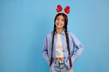 Smiling teenage girl with decorative deer horns and pigtails on blue background.