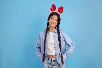 Smiling teenage girl with decorative deer horns and pigtails on blue background.
