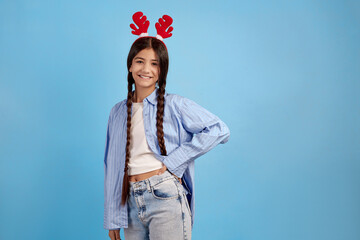 Smiling teenage girl with decorative deer horns and pigtails on blue background.