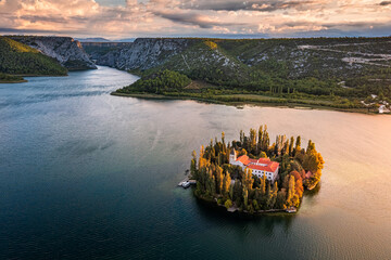 Visovac, Croatia - Aerial view of Visovac Christian monastery island in Krka National Park on a sunny autumn morning with dramatic golden sunrise and clouds and clear turquoise blue water