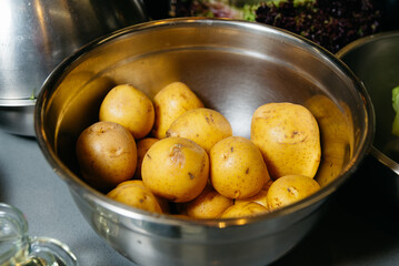 Raw Potatoes in a Metal Bowl for Cooking. A bowl full of unpeeled raw yellow potatoes, a staple ingredient for many recipes, on a kitchen countertop.