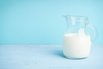 Jug with milk on a wooden light blue background, space for text.