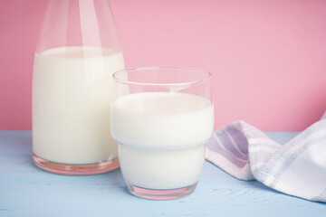 Carafe and glass of fresh milk on a colour background.