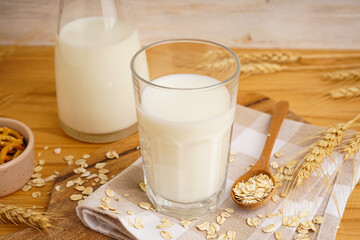 Glass and jug of fresh milk on wooden table against color background.