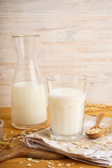 Glass and jug of fresh milk on wooden table against color background. Vertical.