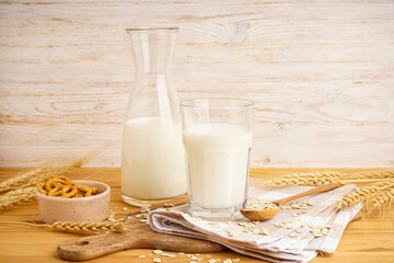 Glass and jug of fresh milk on wooden table against color background.